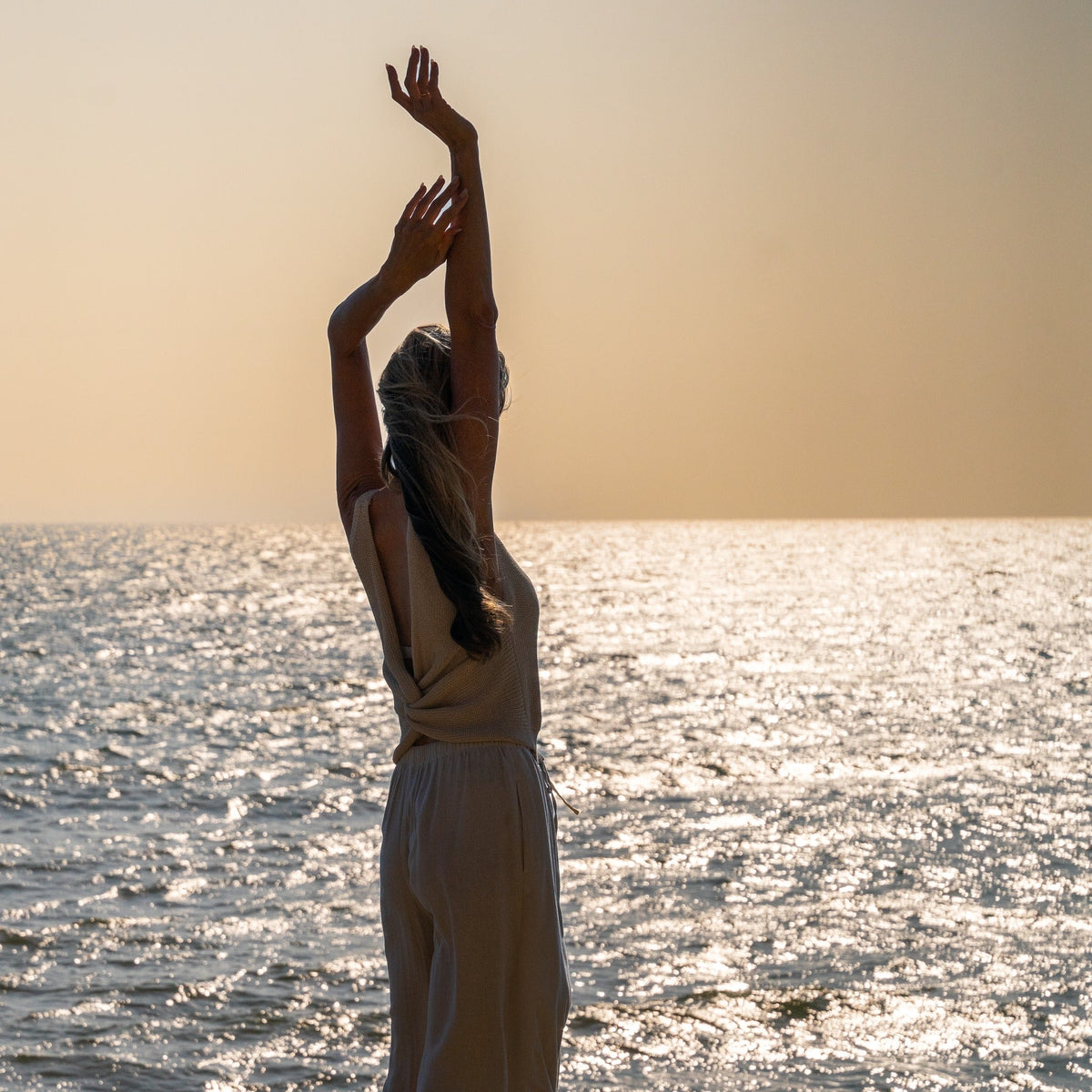 A woman stretching at the coast at golden hour.